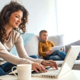 Women on couch on laptop next to her kids.