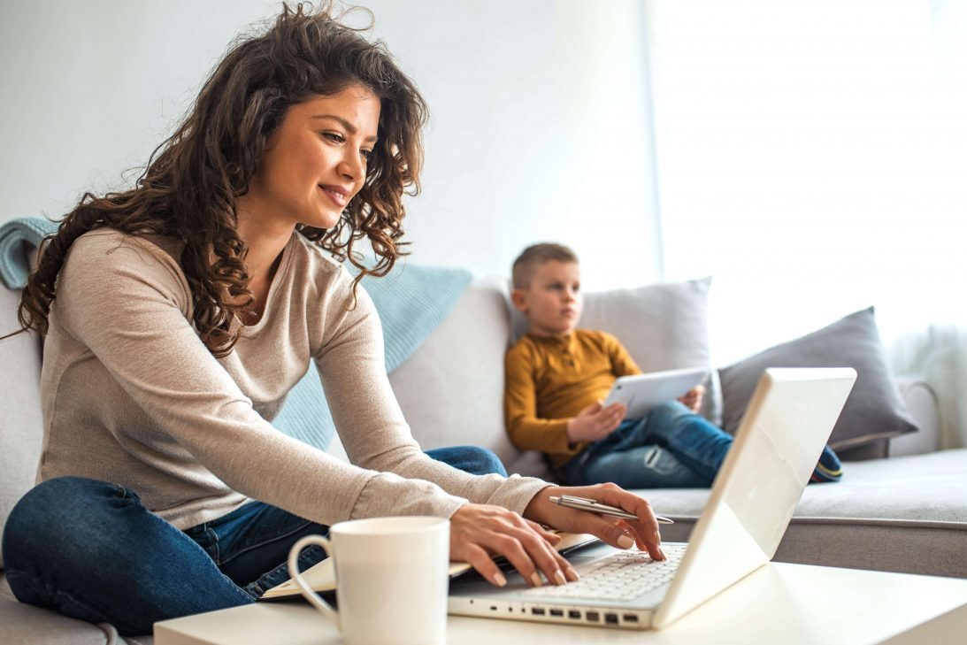 Women on couch on laptop next to her kids.